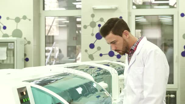 Un giovane assistente di laboratorio segue da vicino il lavoro della centrifuga di laboratorio — Video Stock