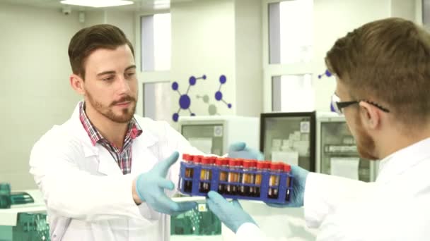 Um técnico de laboratório entrega tubos de ensaio ao seu colega para pesquisas — Vídeo de Stock