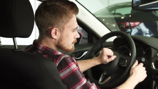 Homem barbudo atraente sorrindo para a câmera sobre seu ombro sentado em um carro novo — Vídeo de Stock