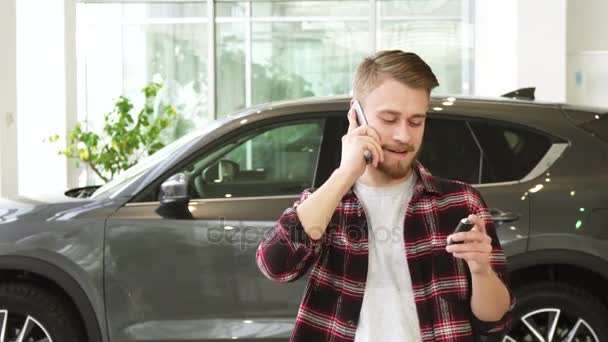 Glücklicher junger Mann telefoniert nach dem Kauf eines neuen Autos im Autohaus — Stockvideo