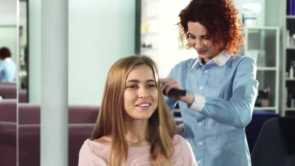 Szczęśliwa młoda kobieta coraz włosy czesane przez profesjonalnego fryzjera w salonie — Wideo stockowe