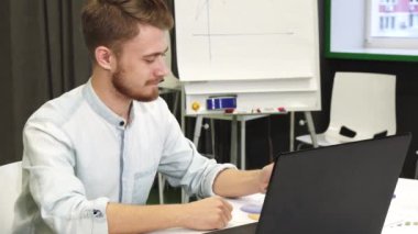 Çekici bir genç adam onun akıllı telefon ve dizüstü bilgisayar ofiste kullanarak