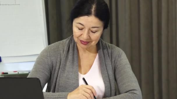 Femme d'affaires senior prenant des notes tout en travaillant sur l'ordinateur portable — Video