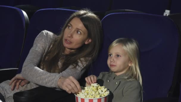 Hermosa mujer y su pequeña hija comiendo palomitas de maíz viendo películas en el cine — Vídeo de stock