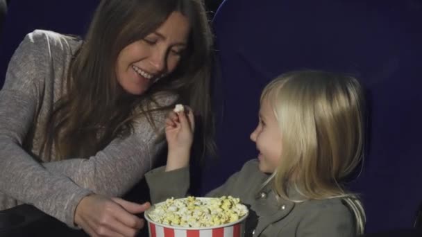 Schattig klein meisje haar moeder vervoederen popcorn in de bioscoop — Stockvideo