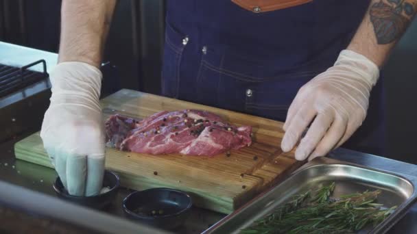 Foto recortada de un chef añadiendo sal a la carne de cerdo antes de cocinar filete — Vídeos de Stock