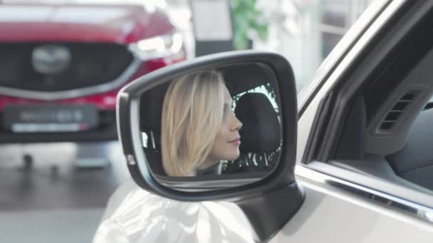 Beautiful happy woman smiling to the camera through side mirror of her car — Stock Video