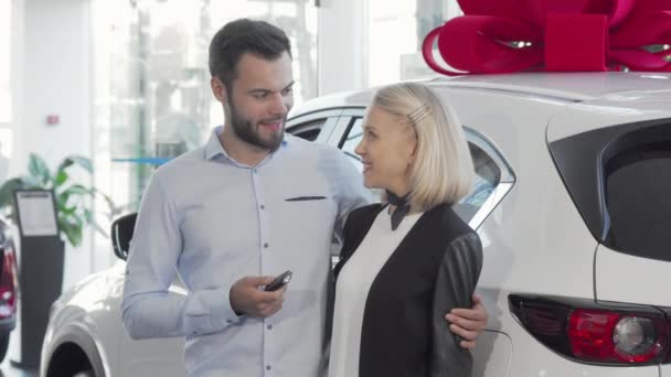 Joyeux jeune couple debout près de leur nouvelle voiture chez le concessionnaire — Video