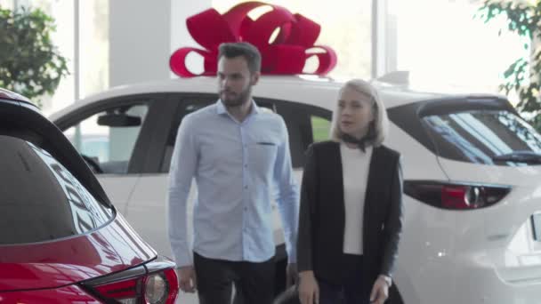 Pareja joven que elige el automóvil para comprar en concesionario de automóviles — Vídeo de stock