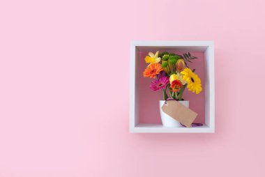 Kutlama kartı olan bahar çiçekleri küp rafında pembe duvar kağıdına karşı sergilenir 