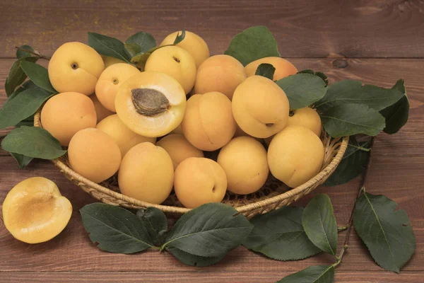 Fresh apricots on a wooden table with a basket — Stock Photo, Image