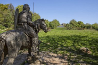 A wood carving of a Norman soldier on horseback looking towards Battle Abbey in East Sussex, UK.  The fields at Battle Abbey are where the Battle of Hastings took place in 1066. clipart