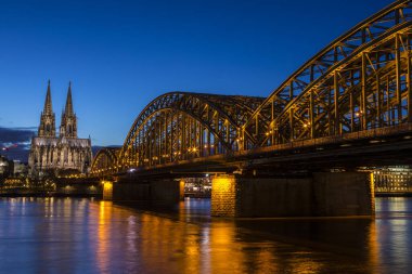 Köln Katedrali ve Almanya 'nın Köln kentindeki Ren Nehri üzerinde uzanan Hohenzollern Köprüsü' nün gece görüşü.