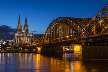 Cologne, Germany - February 17th 2020: A night-time view of Cologne Cathedral and the Hohenzollern Bridge spanning over the Rhine in Cologne, Germany.