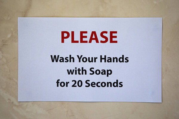 A sign on a bathroom wall saying PLEASE Wash Your Hands with Soap for 20 Seconds.  The recommended length of time to protect yourself from Viruses.
