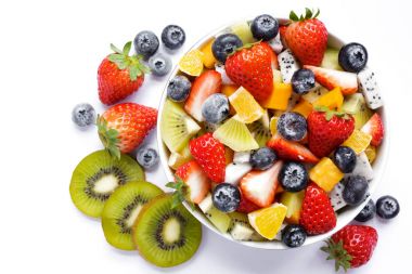 Beyaz zemin üzerine taze meyve sağlıklı salata bir kase. Karışık taze meyve (çilek, portakal, kivi, pitaia, yaban mersini). Yukarıdan görüntülemek.