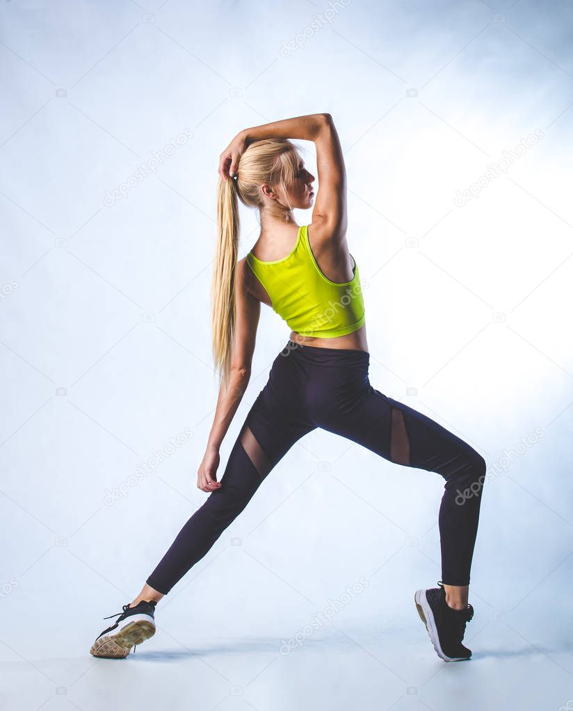 Beautiful female fitness model doing stretches and dancing in a studio, isolated against white background