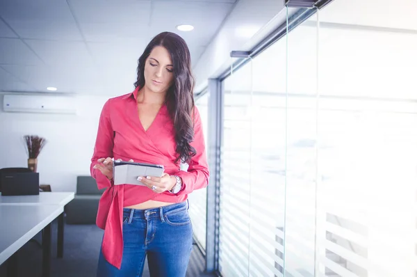 Mooie brunette zakenvrouw permanent in een directiekamer die werken op een tablet-pc — Stockfoto