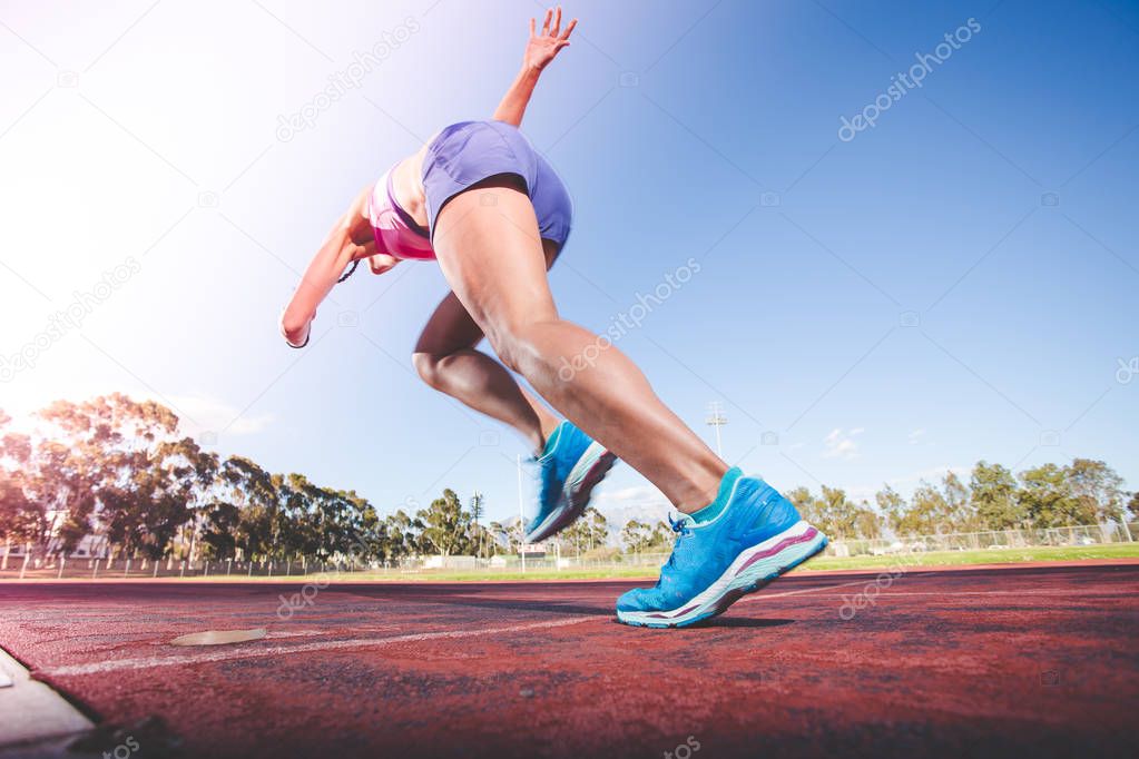 Female fitness model and track athlete sprinting on an athletics track made from tartan