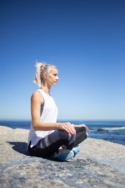 Sarışın kadın modeli meditasyon ve yoga gündüz okyanusa bakan granit kayaya yapıyordum