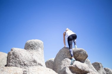 Spor giyim rock rock karşı parlak mavi gökyüzü gündüz atlama içinde güzel sarışın model