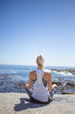 Sarışın kadın modeli meditasyon ve yoga gündüz okyanusa bakan granit kayaya yapıyordum