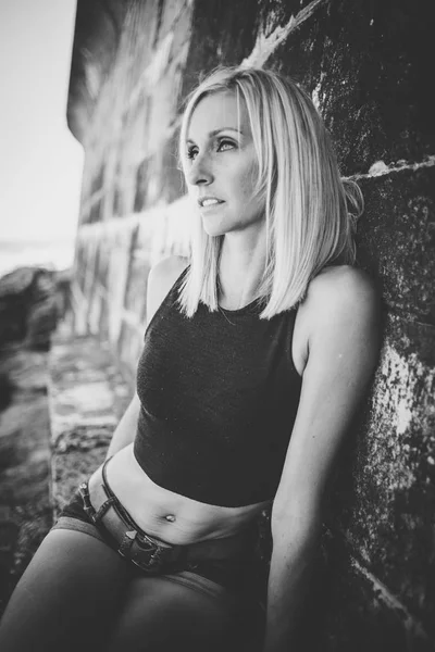 Portrait of blond sporty female model in denim shorts on brick wall background