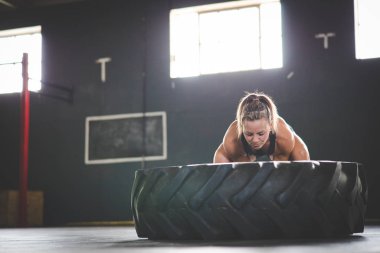 Spor salonunda büyük bir lastikle çapraz egzersiz yapan kadın fitness modeli.