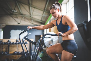 Spor salonunda eliptik bir bisiklette egzersiz yapan bir kadın fitness modeli.
