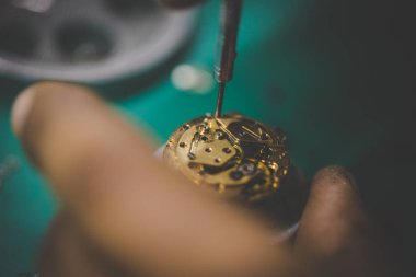 Kırık bir saati hassas araçlarla tamir eden bir saatçinin resmini kapat