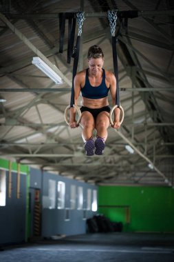 Spor salonunda kadın fitness modeli kendini yukarı çekerek kafa halkaları üzerinde çapraz antrenman yapıyor.