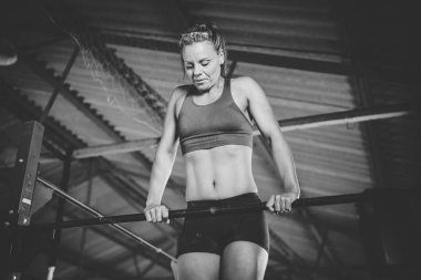 Kadın fitness modeli spor salonundaki barın üstünde barfiks çekiyor.