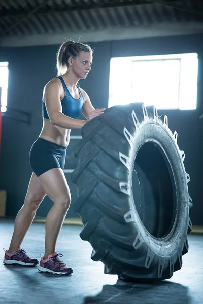 女健身模特儿在体育馆里用一个大轮胎进行交叉体能训练 — 图库照片