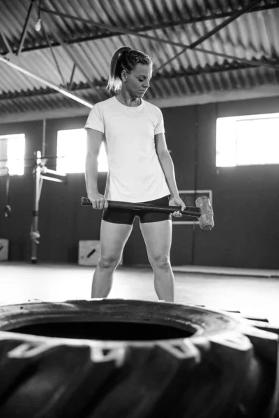 Female fitness model doing cross fit exercise in a gym with a sledge hammer