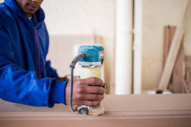 Ahşap mobilya imalathanesinde yönlendirici kullanan bir marangoz resmi.