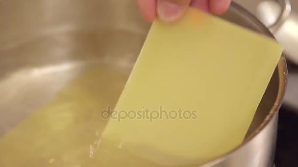 Рука кладет простыни лазаньи в воду — стоковое видео
