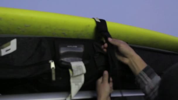 Man zabezpiecza deskę surfingową na dachu jego samochodu — Wideo stockowe