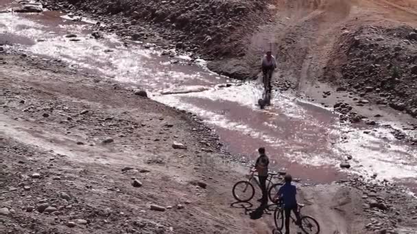 Människor på cyklar som korsar creek i öknen — Stockvideo