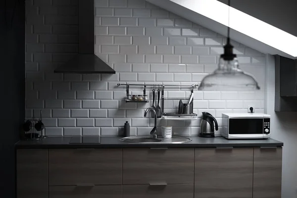 Keuken in de stijl van een loft met beton en bakstenen muren en tegels, een wastafel, vent, magnetron, theepot en een moderne lamp. — Stockfoto