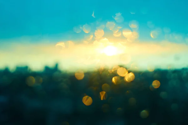 Chuva cai textura no vidro da janela com deslumbrante colorido azul amarelo e luz do pôr do sol verde abstrato embaçado cityscape skyline bokeh fundo. Foco suave . — Fotografia de Stock