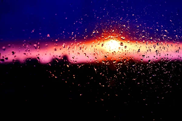 Lluvia gotas textura en vidrio de la ventana con impresionante colorido violeta rosa puesta del sol luz abstracta borrosa paisaje urbano horizonte fondo bokeh. Enfoque suave . — Foto de Stock