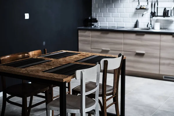 Cocina en estilo loft con paredes y azulejos de hormigón y ladrillo. Hay una mesa de cocina negra con sillas blancas . — Foto de Stock