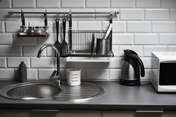 Kitchen in a loft style with concrete and brick walls and tiles, a sink, microwave, teapot and a modern lamp.