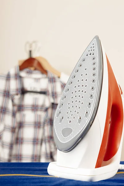 Plancha sobre tabla de planchar contra una pared blanca — Foto de Stock