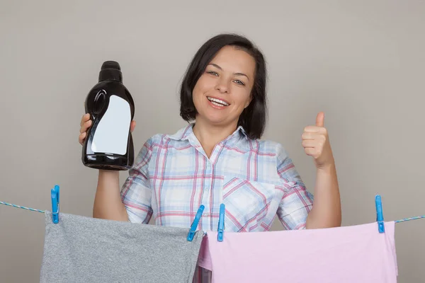 Mujer atractiva con botella de detergente de plástico negro colgando húmedo — Foto de Stock