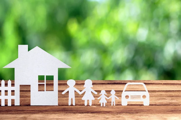 Paper family, house and car on wooden table with garden bokeh ou
