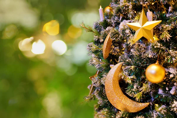 Parlak topları, yıldızı, hilal ayı ve bulanık yeşil ışık arka planında ampulleri olan dekore edilmiş Noel ağacı..                            