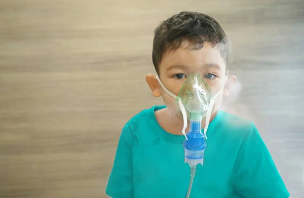 Küçük Asyalı çocuk portresi, gözler ve saçlar kahverengi, hasta çocuk evde nebulizör buharı ile nefes alıyor..