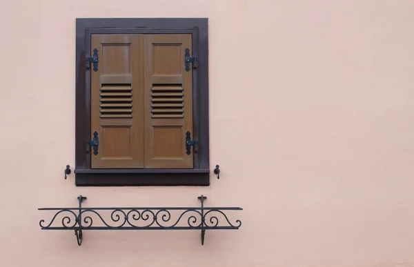 Closed old shutter window with brown doors and an empty metal planter