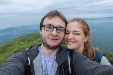 Seyahat eden genç bir çift atış, selfie yaz dağlarda gülümseyen mutlu, spor tarzı giysiler ve sırt çantası, alıp